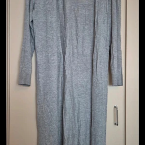 Grå lång kofta från H&M - Säljer en supermysig grå lång kofta från H&M i storlek XS. Perfekt för kyliga dagar med sin långa design och mjuka material. Den har långa ärmar och en öppen front, vilket gör den lätt att matcha med olika outfits. Perfekt för både vardag och mysiga hemmakvällar!