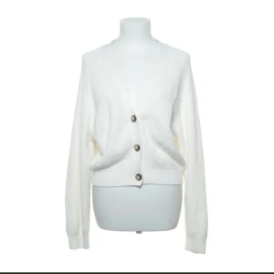 Vit stickad kofta med knappar - Säljer en superfin vit stickad kofta från Monki. Den är croppad med tre stora knappar framtill och har en v-ringad design. Perfekt för höst och vinter.