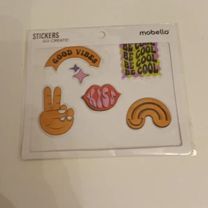 Klistermärken från Mobello - Säljer ett set med coola klistermärken från Mobello. Perfekt för att dekorera din telefon, laptop eller andra tillbehör. Setet innehåller färgglada motiv som 'Good Vibes', 'Be Cool', en peace-hand, läppar och en regnbåge. Gör dina prylar unika och personliga med dessa stickers!