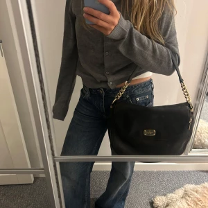 Svart axelväska från Michael Kors - Säljer en snygg svart axelväska från Michael Kors i skinn. Väskan har en elegant design med guldfärgade detaljer och en praktisk dragkedja.