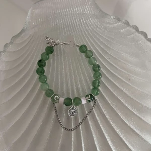 Grönt armband med silverdetaljer - Snyggt armband med gröna pärlor och en silverkedja som detalj. Armbandet har en liten rund berlock i silver med ett mönster. Perfekt för att ge en färgklick till din outfit!