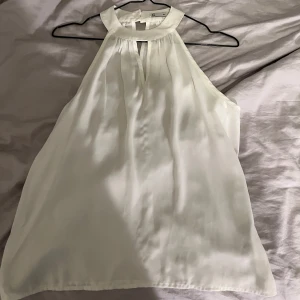 Vit ärmlös blus från Cubus - Säljer en elegant vit ärmlös blus från märket Cubus i storlek 36. Blusen har en rund halsringning med en liten öppning framtill och knäppning i nacken. Perfekt för både vardag och festliga tillfällen!