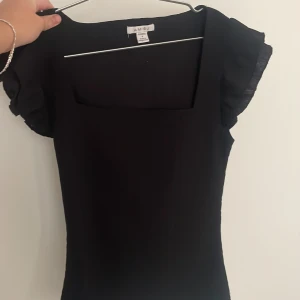 Svart topp från Amisu - Svart topp från amisu  storlek S. Den har en fyrkantig urringning och korta ärmar med volangdetaljer. Perfekt för både vardag och festliga tillfällen.. i bra skick 