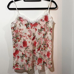 Blommig linne med spetsdetaljer - Säljer ett superfint blommigt linne med tunna axelband och spetsdetaljer vid halsringningen. 