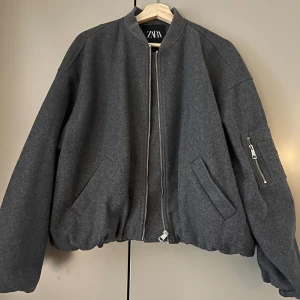 Grå bomberjacka från Zara - Säljer en snygg grå bomberjacka från Zara i mycket bra skick. Jackan har en dragkedja framtill och en cool ficka med dragkedja på ärmen. Perfekt för höst och vår, och den har en normal passform. Superbekväm och stilren!