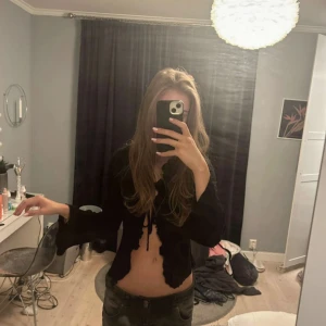 Svart croppad topp med knytning - Säljer en svart croppad topp med knytning framtill. Toppen har långa ärmar och en tight passform, perfekt för en utekväll eller fest. Den är både stilren och trendig, och passar bra till både jeans och kjol. Storlek xs.