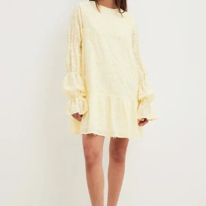 Ljusgul klänning med volanger - Superfin ljusgul klänning med volanger och broderade detaljer. Den har långa ärmar och en söt öppen rygg. Från NA-KD i storlek 34 men passar 36 med