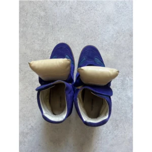 Blå sneakers med unik design - Säljer ett par coola blå sneakers i mocka med en unik design. Skorna har en högre modell med vadderade detaljer och en beige insida. De har en robust gummisula och är perfekta för att sticka ut i mängden. Passar både till vardags och festliga tillfällen.