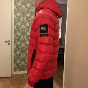 Röd dunjacka från Peak Performance - Säljer en snygg röd dunjacka från Peak Performance. Jackan har en normal passform och är perfekt för kalla vinterdagar. Den har en dragkedja framtill och en praktisk huva. Jackan är i bra skick, 