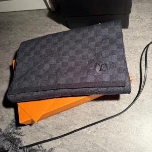 Grå halsduk från Louis Vuitton - Säljer en elegant grå halsduk från Louis Vuitton i ett klassiskt rutmönster. Den är i nytt skick och kommer i sin originalförpackning. Perfekt för vintern och ger en lyxig touch till vilken outfit som helst. Passa på att köpa denna stilrena accessoar!