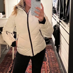 Vit skidjacka  - Säljer en snygg vit pufferjacka i mycket bra skick. Jackan har en dragkedja framtill och praktiska fickor med dragkedjor. Den är långärmad och har en justerbar huva. Passar både höst och vinter. Utrustad med bra fickor för liftkort, telefon osv . Perfekt för skidåkning. 🩷