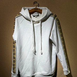 Vit hoodie & byx set - Oäkta set hoodie och matchande byxor. Tjockt och mysigt material i bra kvalité. Både tröjan och byxorna har ett beige band med Guccis logga längs ärmar och ben. Perfekt för en stilren och bekväm look! Normal passform för någon som brukar ha L/XL.