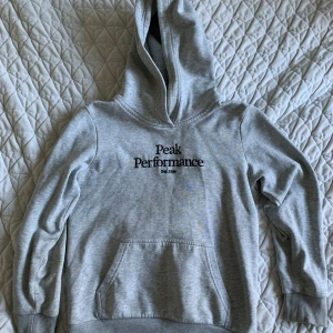 Grå hoodie från Peak Performance 140  - Säljer en snygg och bekväm grå hoodie från Peak Performance. Den har en klassisk design med en känguruficka och justerbar huva. Perfekt för både vardag och träning. Passar bra till höst och vår!