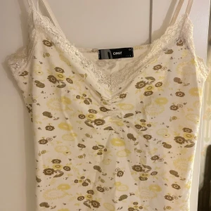 blommigt linne/pościel w kwiaty - Säljer ett sött linne från ONLY i storlek S. Det är vitt med ett gulligt blommönster i gult och brunt. Linnet har spetsdetaljer vid halsringningen och smala axelband. Perfekt för sommardagar!