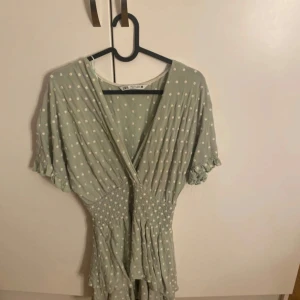 Grön prickig klänning från Zara - Säljer en söt grön klänning från Zara med vita prickar. Den har en omlott-design och korta ärmar med volangdetaljer. Perfekt för vår och sommar! 💚