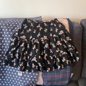Svart blommig kjol - Säljer en superfin svart kjol med blommigt mönster. Kjolen har en volangdetalj som ger den en söt look. Perfekt för vår och sommar! Den är i bra skick och passar perfekt till både vardag,fest och en dag i solen.  Den är helt fantastisk på en tonårig flicka.
