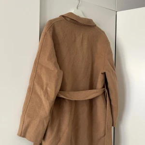Beige kappa från MANGO -  Beige kappa från MANGO i storlek S men passar XS då den känns mindre i storlek. Den har bälte i midjan och långa ärmar 🤗Ca 105 cm lång från axeln och ner.  Ordinarie pris: 1199 kr