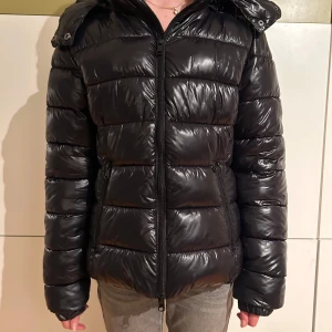 Svart pufferjacka från 157 - Säljer en svart pufferjacka från 157 i storlek XS. Använd ett fåtal gånger men ser ut som ny. Jackan är perfekt för vintern med sin varma och vadderade design. Den har en dragkedja framtill och en mysig huva. Passar både till vardags och lite kyligare äventyr. 🖤