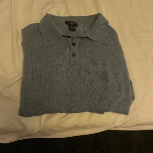 Blå pikétröja från dockers  - Säljer en stilren blå stickad pikétröja med krage och knappar framtill. Perfekt för både vardag och lite mer uppklädda tillfällen. Tröjan har långa ärmar och är i bra skick. Storlek XL men är liten i storleken 