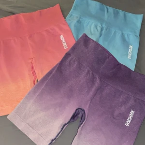 Färgglada träningsshorts från Gymshark - Säljer tre par snygga träningsshorts från Gymshark i olika färger: rosa, blå och lila. De är högmidjade och perfekta för gymmet. Materialet är stretchigt och bekvämt, vilket ger en tight passform. Rosa storlek - S, Blå storlek - XS, lila storlek - M