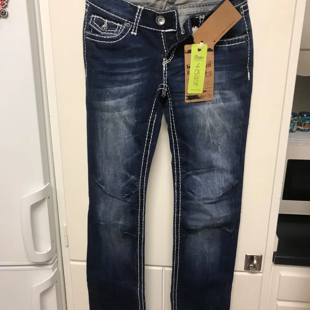 Snygga mörkblå jeans från Soccx i nytt skick. De har en cool kontrastsöm och knappar med logga. Perfekt för vardagsstilen med en normal passform och låg midja. Materialet är slitstarkt denim, vilket gör dem både bekväma och hållbara. Passar perfekt till både sneakers och boots!. Jeans & Byxor.