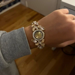 Glittrig guldfärgad klocka - Säljer en superfin guldfärgad klocka med stenar, en av stenarna är halvt borta och en är lite sne som man kan se på bilden men det är inget man tänker på när man har på sig den🤍 
