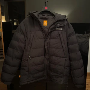 Svart dunjacka från Timberland - Säljer en svart dunjacka från Timberland i mycket bra skick. Jackan har en dragkedja och är perfekt för kalla vinterdagar.Funkar också för L. Modellen är 182cm och väger 82kg.