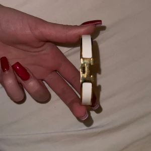 Elegant vitt och guld armband - Säljer ett superchict armband i vitt och guld. Det har en stilren design med en ikonisk H-detalj i mitten. Perfekt för att ge en touch av lyx till vilken outfit som helst. Passar både till vardags och fest. Ett måste för alla som älskar stilrena smycken!