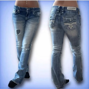 Jättesnygga Rock Revival Jeans! - Säljer ett par snygga blå bootcut jeans med slitningar och coolt broderi på bakfickorna. De är lågmidjade och har en avslappnad passform. Perfekta för en casual look eller en utekväll. Passar bra med både sneakers och klackar! Köpa på plick men säljer då de var för stora🩵