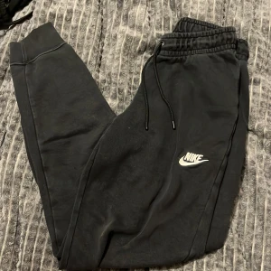 Svarta mjukisbyxor från Nike - Säljer ett par svarta mjukisbyxor från Nike i bra skick. De har en elastisk midja med snörning och en broderad Nike-logga på benet. Perfekta för en avslappnad stil eller träning. Superbekväma och stilrena!