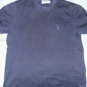 AMI Paris T-Shirt - Säljer en snygg mörkblå t-shirt från AMI i bra skick. Den är kortärmad och har en liten broderad logga på bröstet och nacken. Sparsamt använd kondition 8/10. Har sett många förfalskade t-shirts från AMI men kan själv verifiera äktheten med ett kvitto