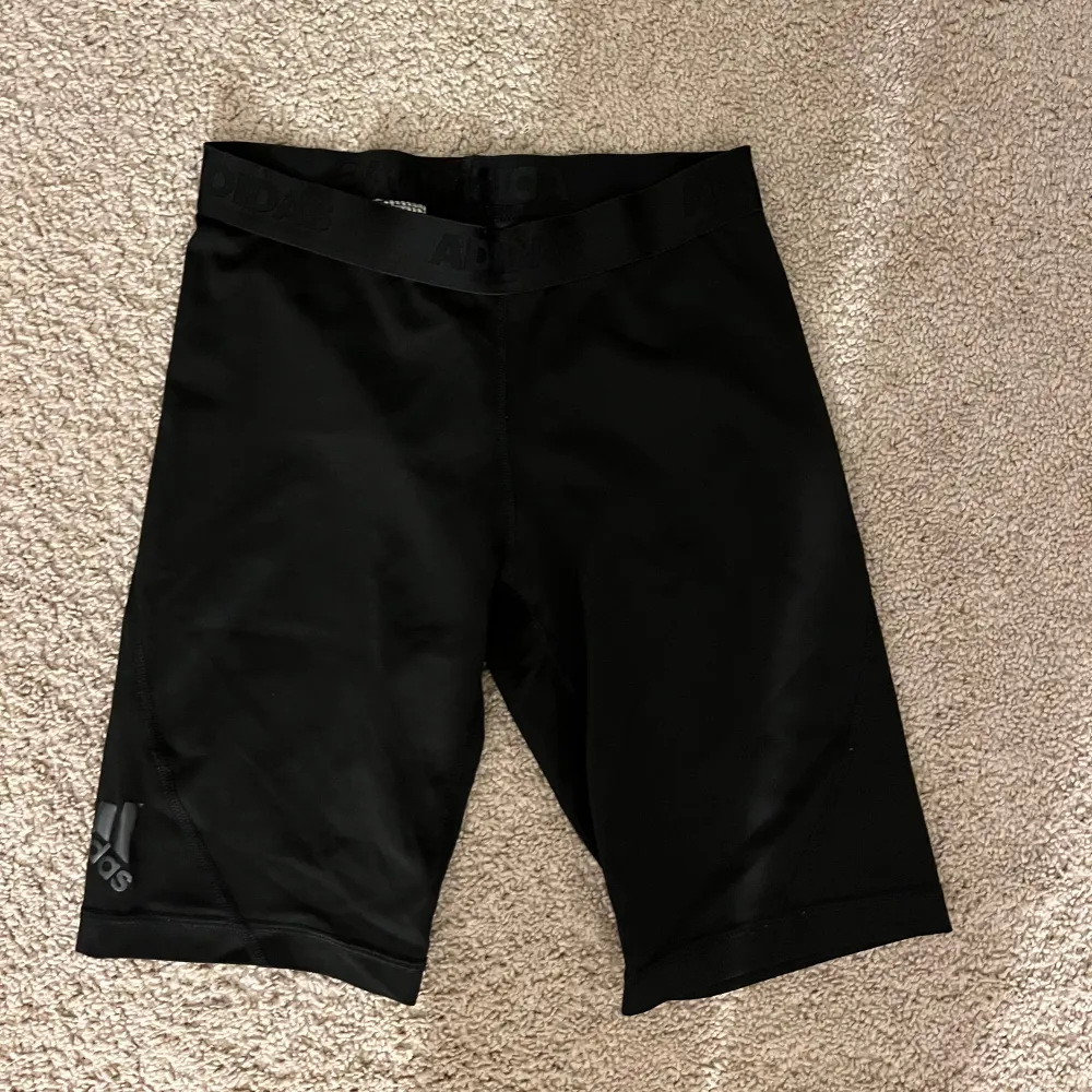 Säljer ett par svarta träningsshorts från Adidas i mycket bra skick. De är tillverkade i ett lätt och stretchigt material, perfekt för intensiva träningspass. Shortsen har en normal passform och en elastisk midja för extra komfort. Adidas-loggan syns diskret på benet.. Shorts.