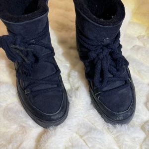 Marinblå boots från Inuikii - Säljer dessa populära marinblå INUIKII vinterboots i bra skick i storlek 38. De är små i storleken så de passar dig som har 37 också. De är gjorda av mocka och skinn och har en mysig, fodrad insida för extra värme. Skorna har den klassiska snygga Inuikii-snörningen framtill och är perfekta för kalla höst- och vinterdagar.