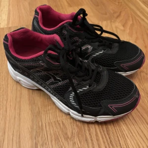 Svarta och rosa träningsskor  - Säljer ett par snygga svarta träningsskor med rosa detaljer och vit sula. De har en sportig design med snörning och är perfekta för träning eller vardagsbruk. Skorna har en bekväm passform och är i bra skick. Perfekta för dig som vill ha stil och komfort i ett!