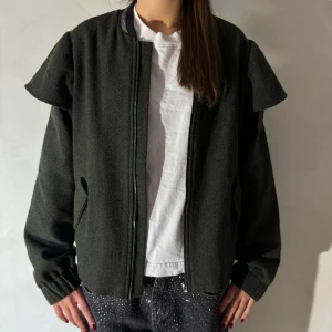 Mörkgrön bomberjacka - Säljer en snygg mörkgrön bomberjacka med volang i normal passform. Jackan har långa ärmar och en dragkedja framtill. Perfekt för höst och vår, med en stilren look som funkar till det mesta. Den är i bra skick och redo för nya äventyr!