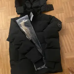 Säljer en svart pufferjacka från Canada Goose i mycket bra skick. Jackan är perfekt för vintern med sin tjocka vaddering och långa ärmar. Den har en hög krage och en praktisk dragkedja framtill. Perfekt för kalla dagar! 🖤