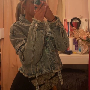 Jeansjacka i croppad stil - Säljer en snygg croppad jeansjacka med slitna detaljer och knappar framtill. Perfekt för en avslappnad look och passar bra till både vardag och fest. Jackan har långa ärmar och en klassisk krage.