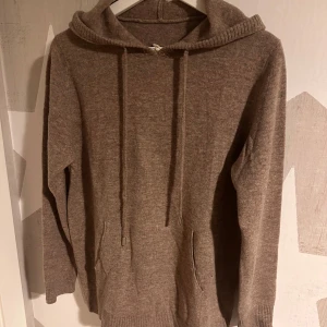 Brun hoodie i kashmir - Säljer en supermjuk och varm brun hoodie i kashmir. Perfekt för kyliga dagar med sin avslappnade passform och praktiska fickor. Den har långa ärmar och en klassisk huva med dragsko. Passar både till vardags och mysiga hemmakvällar. Säljes pga den är för stor 