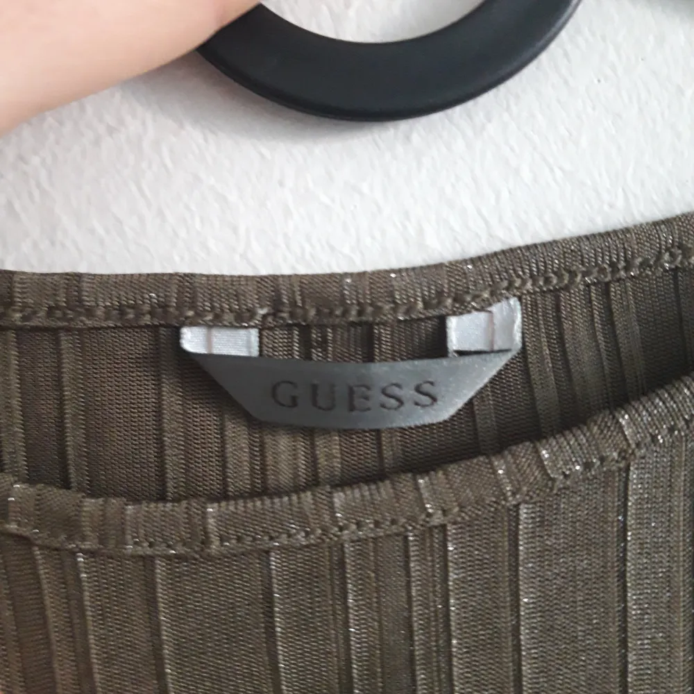 Snygg glittrig topp från Guess (strl S) i en metallisk grön-brun nyans. Den är ärmlös och har ett ribbat mönster med Guess-loggan i glittriga stenar på framsidan. Perfekt för en festlig kväll eller en utekväll med vänner. Toppen är stretchig och framhäver figuren.. Yläosat.