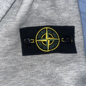 Grå hoodie från Stone Island - Säljer en snygg grå hoodie/kofta från Stone Island i bra skick. Den har en dragkedja framtill och en klassisk logga på ärmen. Perfekt för både höst och vår, och den är superbekväm att ha på sig. Passar till alla tillfällen!