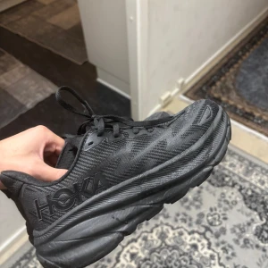 Helt nya  sneakers från Hoka - Säljer ett par svarta Hoka sneakers i helt nytt skick. De har en robust sula och snyggt mönstrad ovandel. Perfekta för både träning och vardagsbruk. Skorna har snörning för en säker passform.