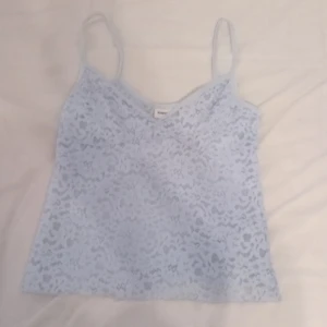 Ljusblå spetslinne - Säljer ett supergulligt ljusblått spetslinne. Perfekt för sommardagar eller att ha under en kavaj för en chic look. Det är ärmlöst med smala axelband och har en v-ringad design. Passar både till vardags och fest!