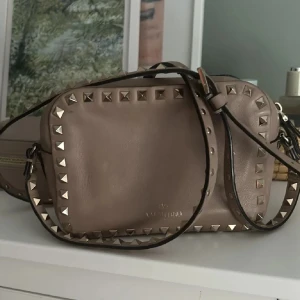 VALENTINO CAMERA BAG BEIGE/ROSA 🩷 - Säljer denna då jag tyvärr inte använder den längre! Den är i relativt bra skick men är lite smutsig inuti och har tappat färg på en nit. Har tyvärr inte kvitto men har dustbag och den är garanterat äkta 💕 hör av dig för fler frågor eller bilder 