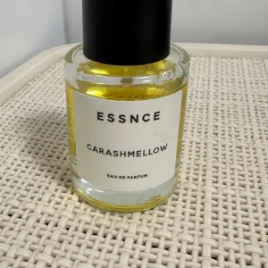 Carashmellow Eau de Parfum från Essnce - Säljer en flaska Carashmellow Eau de Parfum från Essnce. Flaskan är genomskinlig med en svart kork och innehåller en gyllengul vätska. Den har en stilren etikett med svart text. Perfekt för dig som älskar söta och mjuka dofter!