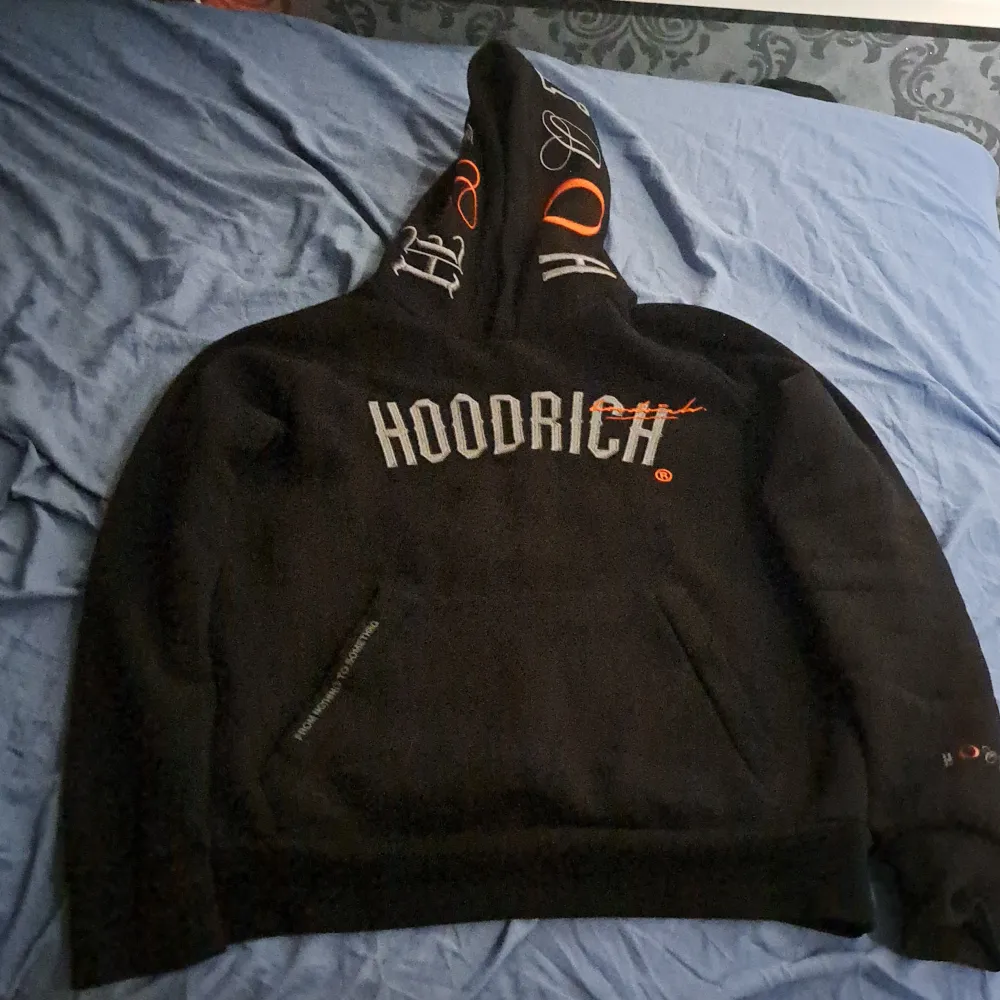 Säljer en svart hoodie från Hoodrich med coola detaljer. Den har en stor logga på framsidan och text på baksidan. Perfekt för att hålla sig varm och stilren. Passar till alla tillfällen!. Tröjor & Koftor.