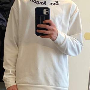 Säljer en stilren vit sweatshirt med texten 'Los Angeles' tryckt i svart på bröstet. Tröjan har en normal passform och är perfekt för både vardag och chill. Den är gjord i ett mjukt och bekvämt material som håller dig varm under kyligare dagar.