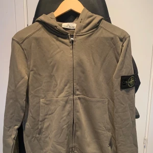 Grå hoodie från Stone Island - Säljer en snygg gr hoodie från Stone Island. Den har en dragkedja framtill och en klassisk huva. På ärmen finns det ikoniska Stone Island-märket. Perfekt för höst och vår, och den är i bra skick. Passar både till vardags och lite mer avslappnade till
