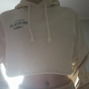 Beige croppad hoodie med tryck - Säljer en supercool beige croppad hoodie med tryck både fram och bak. Den har en luva och dragsnören, perfekt för en avslappnad stil. Trycket på ryggen är riktigt unikt och ger en edgy vibe. Perfekt för höst och vår!