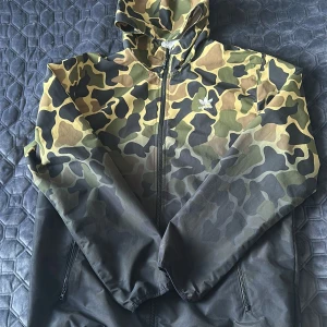 Adidas tunn regnjacka - Säljer en Adidas tunn regnjacka i bra skick, storlek L för herr. Jackan är idealisk för blåsiga och regniga dagar, med ett lätt och smidigt material som håller dig torr utan att bli för varm. Perfekt för både sport och vardag med den klassiska stilen