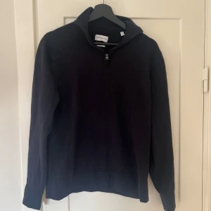 Mörkblå merinoulltröja från These Glory Days - Säljer en stilren blå tröja från These Glory Days i Superior Merino. Tröjan har en dragkedja vid halsen och långa ärmar, perfekt för kyliga dagar. Den är i storlek L och passar både till vardags och lite finare tillfällen. Krympt lite, sitter som M